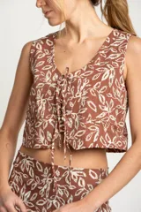 Chaleco marrón con estampado de hojas blancas, escote en V y lazo ajustable en el centro.