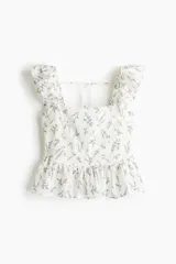 Blusa blanca con estampado floral en tonos lavanda, de tela ligera, con escote recto, breteles anchos con volados, espalda escotada con tiras finas horizontales que se atan en la parte superior, sección de punto smock en la espalda baja, costura fruncida en la cintura y peplum con vuelo.