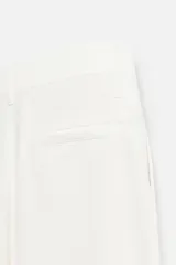 Pantalón blanco de corte relajado con pliegues frontales, bolsillos laterales y bolsillos traseros de vivo. Cierre frontal con cremallera y botón.