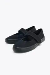 Zapato plano tipo bailarina en tejido color negro. Detalle de pespunte en el cuerpo, tira con adhesivo ajustable, suela engomada y acabado en punta redonda.