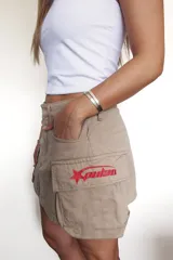 Minifalda color beige con bolsillos tipo cargo y bordado rojo con forma de estrella y texto en el bolsillo lateral.