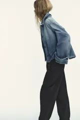 Chaqueta de denim celeste con cuello alto, manga larga con trabilla y bolsillos laterales. Presenta detalle de pliegues en la espalda y cierre frontal con botones ocultos.