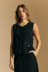 Chaleco negro de vestir con cuello solapa y cierre frontal de botones. Presenta costuras contrastantes blancas que definen el diseño y bolsillos delanteros. Se combina con una camisa blanca de manga larga.