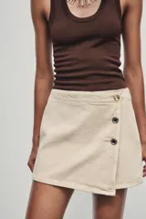 Falda pantalón corta color crudo, de tiro alto con delantero cruzado y cierre con cremallera oculta y botones.
