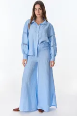 Camisa celeste de lino con cuello clásico, abotonada al frente y mangas largas con detalle de puntilla en los hombros.