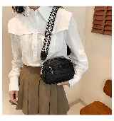 Cartera bandolera negra de cuero sintético con correa ancha de tela estampada.