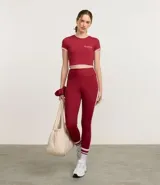 Remera deportiva cropped de manga corta, color rojo oscuro, con cuello redondo y ribetes contrastantes en blanco en el cuello y los puños. Presenta una pequeña inscripción en el pecho.