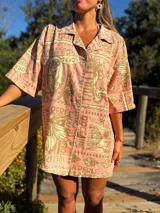 Camisa oversize de manga corta con cuello camisero y botones frontales. Confeccionada en tejido estampado con motivos marinos y texto en tonos rosados y beige.