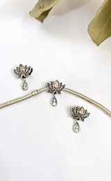 Dije charm plateado con forma de flor de loto y una piedra color rosa en el centro. Incluye un dije colgante en forma de lágrima con incrustaciones de strass.
