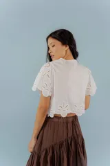 Blusa negra con bordado calado, escote en V con lazos para atar y mangas cortas abullonadas.