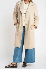 Tapado largo color beige claro, de corte oversize, con cuello solapa y cierre frontal de botones.