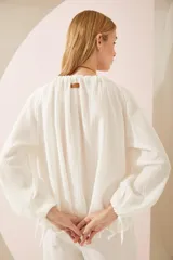 Camisa oversize blanca de lino, con cuello en V, mangas largas abullonadas con puños elásticos y lazos decorativos.
