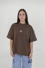 Remera marrón de corte holgado con cuello redondo y mangas cortas. Estampado frontal pequeño con el texto "pulau" y tres estrellas rojas.