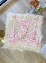 Conjunto de lencería rosa de encaje floral, compuesto por un corpiño triangular con breteles regulables y cierre frontal, y una tanga regulable.