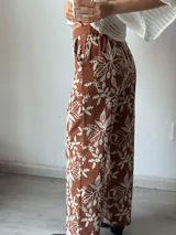 Pantalón de tela color terracota con estampado de hojas y flores en color blanco.