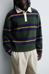 Polo de punto de corte relajado con diseño de rayas horizontales en tonos verde, azul y mostaza. Presenta cuello solapa en color crema a contraste y cierre frontal con tres botones.