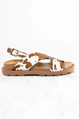 Sandalias con tiras cruzadas de cuero con estampado animal print de vaca en tonos marrón y blanco. Tira trasera con hebilla ajustable. Suela plana color marrón.