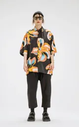 Camisa de manga corta negra con estampado de flores grandes en tonos amarillo, naranja y celeste. Corte oversize con canesú en la espalda.