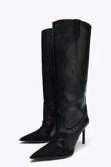 Bota alta de cuero sintético negro con detalles de pespuntes en contraste y puntera de gamuza. Tiene taco fino y tiradores laterales.
