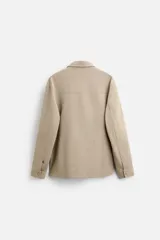 Sobrecamisa negra de tejido con elasticidad, cuello solapa y manga larga acabada en puño con botón a presión. Tiene bolsillos de plastrón en el pecho y cierre frontal con botones a presión.