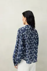 Camisa blanca con bordado floral en contraste, cuello mao, abotonadura frontal y mangas largas con frunces en los hombros.