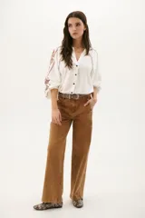Camisa blanca de manga larga con bordados marrones en hombros y mangas, cuello en V y cierre frontal con botones.