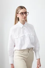 Camisa blanca de algodón con diseño utilitario y calce relajado. Presenta dos bolsillos frontales de estilo cargo con tapa y costuras a contratono.