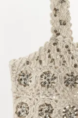 Sujetador de crochet color crudo con escote recto y tirantes anchos. Detalle de abalorios y lentejuelas combinados a contraste. Cierre en espalda con lazada en mismo tejido.