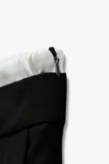 Pantalón negro de tiro alto con doble cintura elástica ajustable con cordón y tejido combinado. Pinzas frontales, bolsillos delanteros y falso bolsillo de vivo en espalda. Pernera ancha.