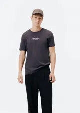 Camiseta blanca de algodón con cuello redondo y mangas cortas. Estampa rectangular con borde negro que contiene la frase "NATURAL ATMOSPHERE" en letras mayúsculas y una imagen de montañas y mar.