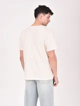 Remera color crudo con estampa frontal de estilo western con texto y paisaje desértico.