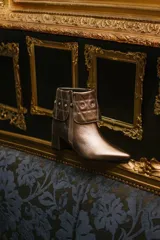 Botas cortas color peltre con taco cuadrado, capellada de cuero y cuello con diseño capitoné y apliques brillantes.