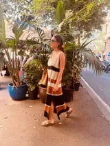 Vestido largo tejido a rayas horizontales en tonos crudo, tostado y negro, con breteles finos y abertura lateral.