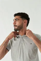 Remera tipo polo gris con cuello y mangas con ribete negro y logo bordado en el pecho.