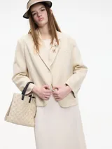 Blazer color crema con textura a rayas y lentejuelas. Tiene cuello con solapas, cierre frontal con botones, bolsillo en el pecho y apliques florales. Confeccionado en algodón y poliéster.