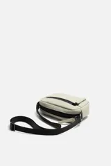 Bandolera negra de acabado engomado con correa ajustable y extraíble. Tiene un compartimento principal con cierre de cremallera, un bolsillo interior con cremallera y un bolsillo frontal con cremallera.