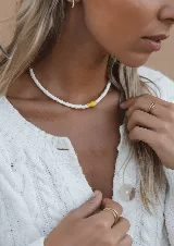 Collar corto de cuentas de caracol blancas con un dije de pez amarillo de cerámica.