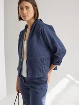 Chaqueta azul de lino con cierre frontal con cremallera, capucha y bolsillos laterales.