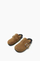 Zueco color beige con hebilla metálica ajustable, confeccionado en material símil gamuza y suela de goma negra.