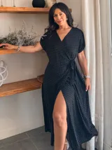 Vestido negro de largo midi con estampado de pequeños puntos blancos, escote cruzado en V, mangas cortas tipo mariposa y lazada ajustable en la cintura. Presenta una abertura frontal pronunciada en la falda.