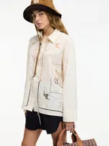 Camisa color crema con bordados y calados en el frente y la espalda, cuello camisero, botones frontales y mangas largas con puños abotonados.
