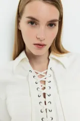Vestido corto de denim color blanco, con cuello camisero, mangas cortas, dos bolsillos frontales y ajuste con cordones cruzados en el escote.