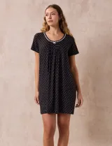 Camisón corto negro con lunares blancos, de tejido suave y escote redondo con detalle plisado y moño blanco.