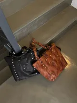 Bolso tote grande de cuero color marrón con apliques metálicos plateados.