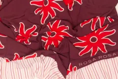 Pareo rectangular de viscosa con estampado de flores rojas sobre fondo borgoña y borde inferior con rayas verticales rojas, amarillas y blancas.