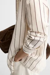 Camisa de hombre regular fit, color blanco con rayas verticales negras, cuello solapa, manga larga con puños abotonados y cierre frontal con botones.