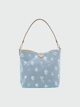Bolso tipo cubo Longchamp modelo Le Roseau Denim, color gris oscuro con estampado de flores blancas. Tiene asa corta de cuero marrón y cierre con botón a presión. Incluye correa larga extraíble y ajustable.