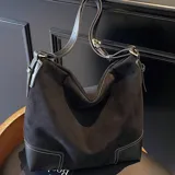 Bolso tipo hobo o tote de eco cuero con textura símil gamuza en color negro. Presenta detalles de pespuntes en color blanco en la base, que es de cuero liso negro. Tiene correa de hombro delgada y ajustable.