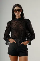 Blusa negra de manga larga con cuello alto y textura transparente con apliques florales en relieve.