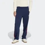 Pantalón deportivo Adidas Firebird azul marino con rayas rojas y blancas en los laterales y logo dorado bordado. Confeccionado en tejido de tricot de poliéster reciclado, con corte clásico y cintura elástica ajustable con cordón.